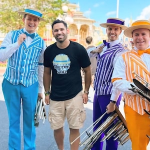 May include: Five men wearing matching striped waistcoats and hats, holding musical instruments. One man is wearing a black t-shirt with the text "Dapper Dan" on it.