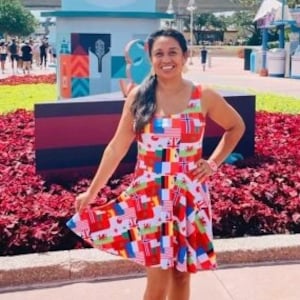 Puede incluir: Un vestido sin mangas hasta la rodilla con un estampado integral de varias banderas internacionales en colores vibrantes. El vestido tiene un escote redondo y una falda acampanada, combinado con zapatillas deportivas azul oscuro con suela blanca.