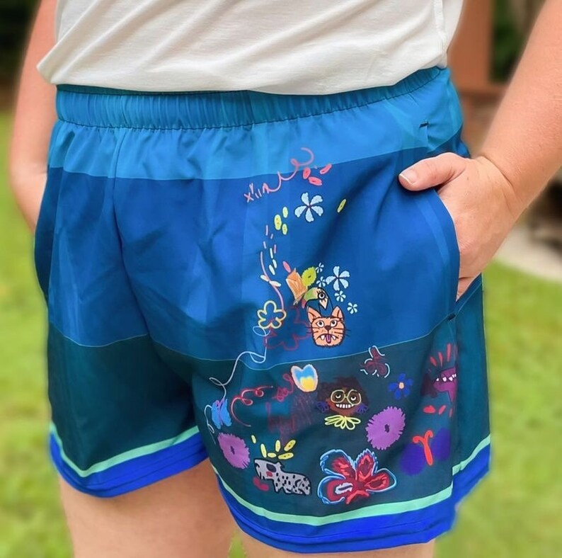 May include: Blue running shorts with a colorful, whimsical print featuring flowers, animals, and the word "xlin".