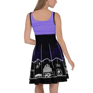 May include: A purple and black skater dress with a white silhouette of a haunted house and other spooky attractions. The dress has a purple striped bodice and a black skirt with a white silhouette of a haunted house and other spooky attractions.