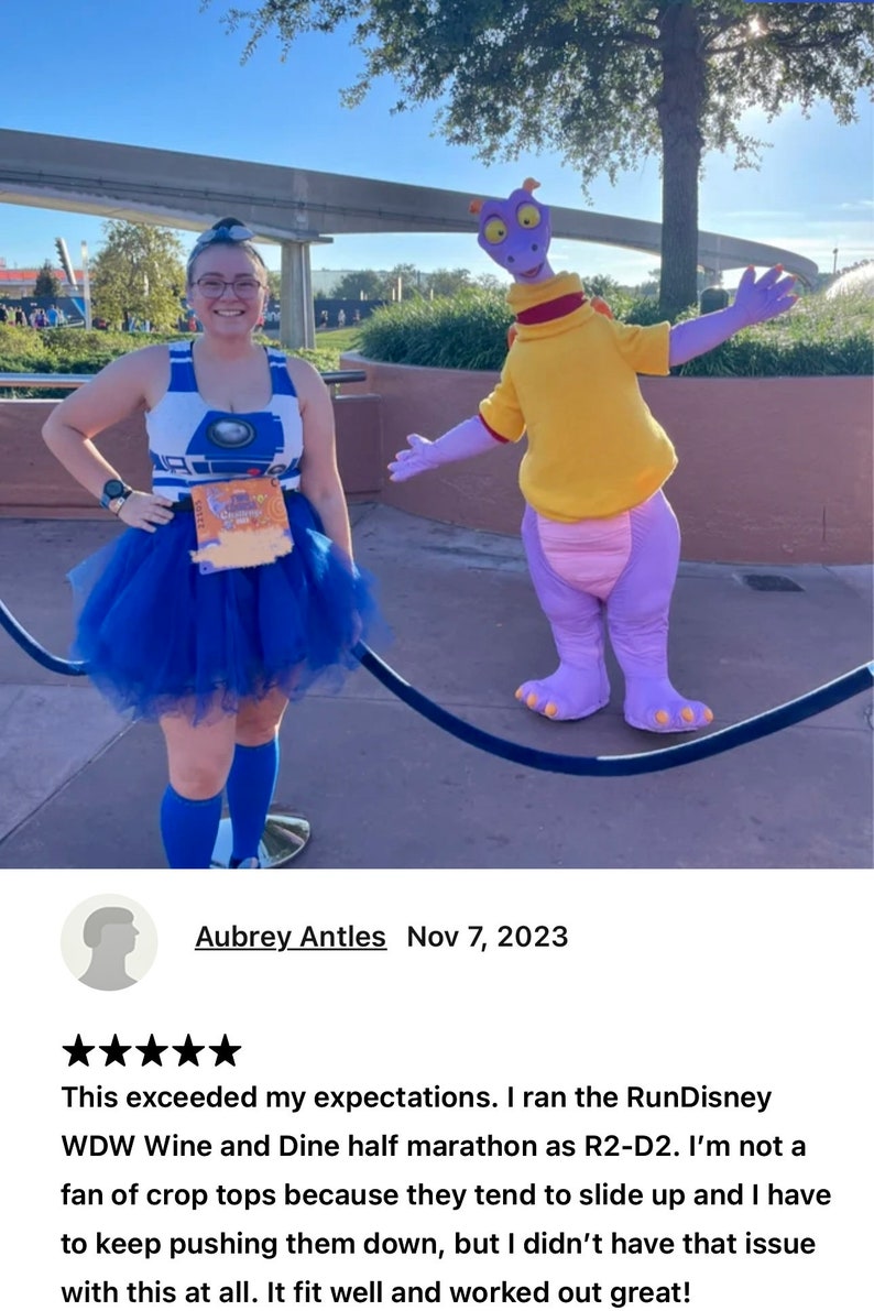 May include: A woman wearing a blue and white crop top with a blue tutu skirt and blue socks poses with a purple character dressed in a yellow shirt. The woman is holding a race bib that says "Wine & Dine Half Marathon".
