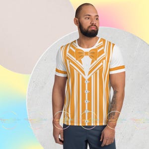 May include: White short-sleeved t-shirt with a mustard yellow and white striped vest design, featuring a bow tie and button details. The shirt has a crew neck and short sleeves. The design is printed on the front of the shirt.