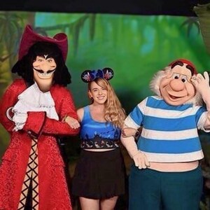 以下が含まれることがあります： ディズニー映画「ピーターパン」のキャラクターに扮した3人が写真に写っています。一人は赤いコートを着たフック船長、もう一人は青いトップスと黒いスカート、もう一人は青と白のストライプのシャツを着たスミーです。