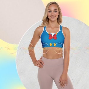 May include: Blue sports bra featuring a design inspired by Donald Duck. The bra has a white trim, a red bow tie, and yellow button details. The bra is paired with light pink leggings.