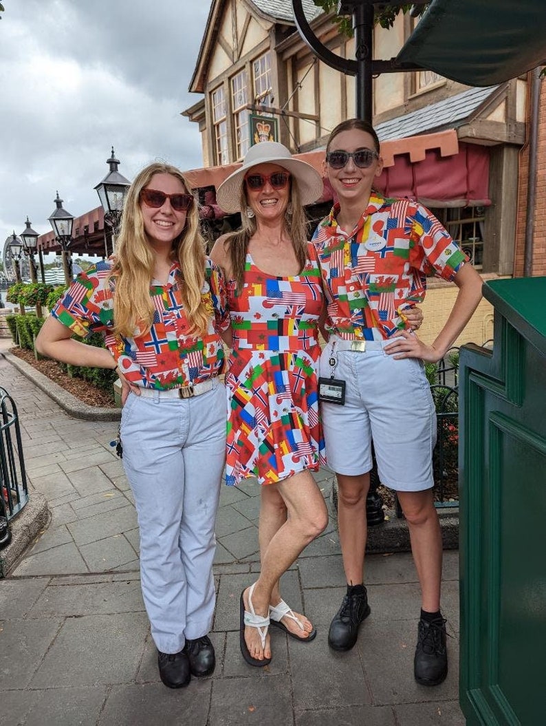 Puede incluir: Dos camisas de manga corta con botones y un vestido sin mangas, todos con un patr&oacute;n vibrante y multicolor de varias banderas internacionales. Las camisas se combinan con pantalones y pantalones cortos claros, mientras que el vestido se usa solo.