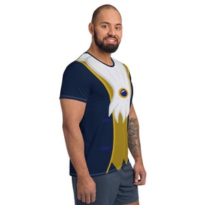 May include: A navy blue t-shirt with a printed design of a gold and white tuxedo vest with a blue jewel. The t-shirt has short sleeves.