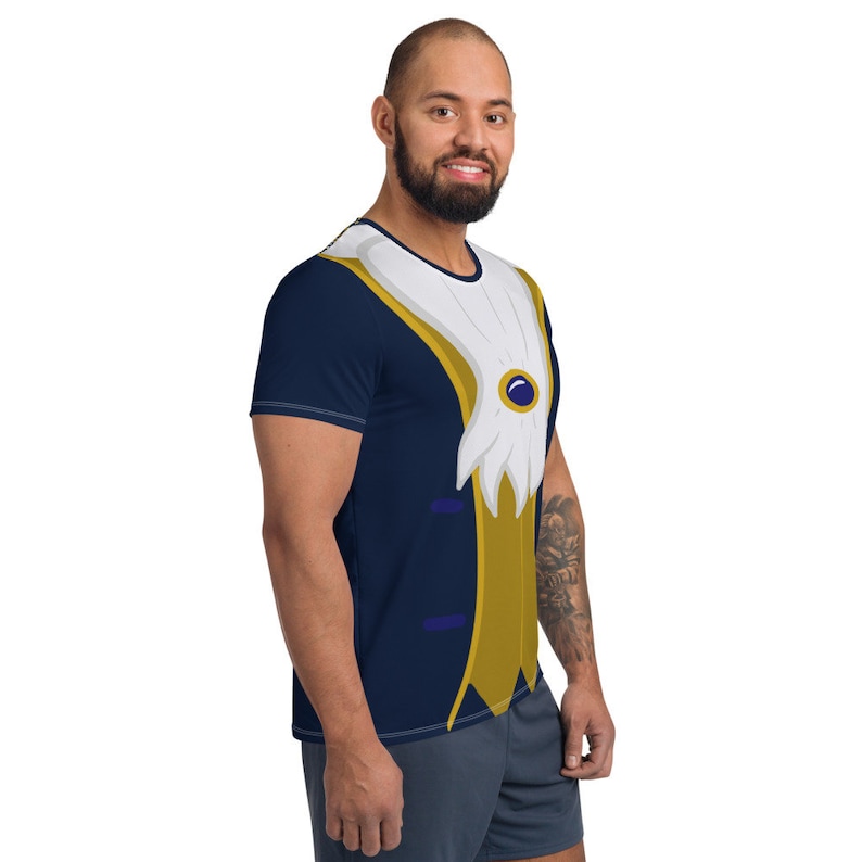 May include: A navy blue t-shirt with a printed design of a gold and white tuxedo vest with a blue jewel. The t-shirt has short sleeves.