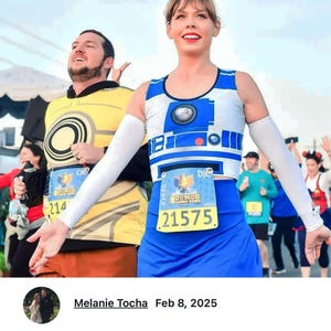 May include: Two people wearing running outfits with race numbers. The woman is wearing a blue and white R2-D2 themed running top and a blue skirt. The man is wearing a yellow running top with a circular design. The woman's race number is 21575 and the man's race number is 214.