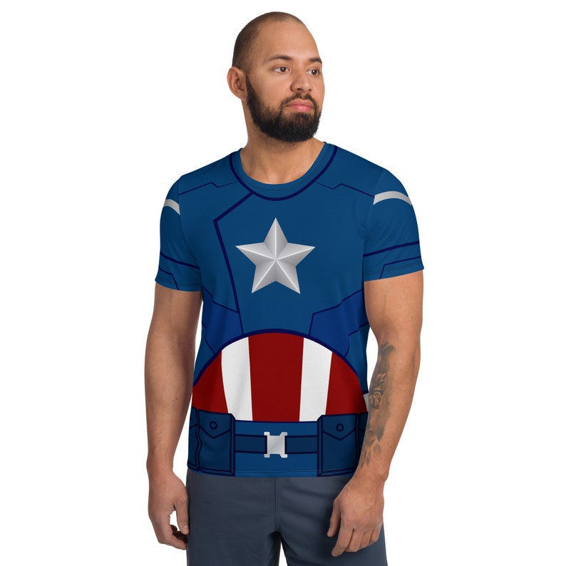 May include: A blue and red t-shirt with a white star and a red, white, and blue shield design. The shirt is a superhero costume.