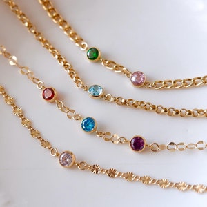 May include: Five gold chains with colorful gemstones. The chains are layered on top of each other and have different styles of links. The gemstones are red, pink, green, blue, and purple.