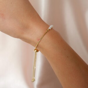 Puede incluir: Un brazalete de cadena dorada con cierre deslizante y detalles de perlas blancas.
