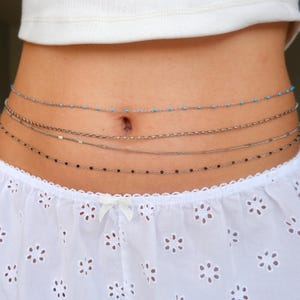Peut inclure: Un ensemble de quatre cha&icirc;nes de taille superpos&eacute;es port&eacute;es autour de la section m&eacute;diane. La cha&icirc;ne sup&eacute;rieure pr&eacute;sente de petites perles turquoise, suivie d'une cha&icirc;ne argent&eacute;e textur&eacute;e, d'une fine cha&icirc;ne &agrave; maillons et d'une cha&icirc;ne inf&eacute;rieure orn&eacute;e de minuscules perles noires.