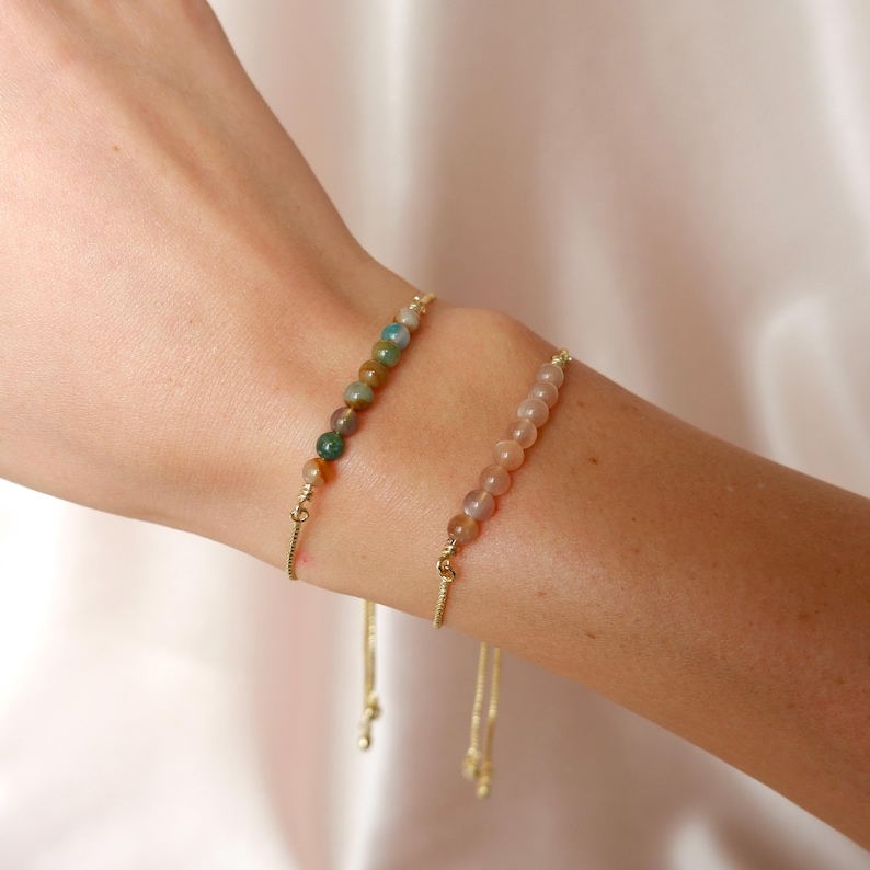 Puede incluir: Dos delicados brazaletes de cadena dorada con nudos deslizantes ajustables. Un brazalete presenta una fila de peque&ntilde;as piedras redondas multicolores, mientras que el otro brazalete presenta una fila de peque&ntilde;as piedras redondas de color rosa claro.