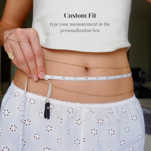 May include: Gold-colored body chain with a measuring tape. The text "Custom Fit" and "type your measurement in the personalization box" are displayed. The model is wearing a white top and skirt.