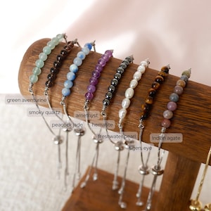 Könnte beinhalten: Ein Set aus zehn verstellbaren Edelstein-Armbändern mit silbernen Schnüren. Die Armbänder sind mit grünem Aventurin, Rauchquarz, Pfauenjade, Amethyst, Hämatit, Süßwasserperlen, Tigerauge, indischem Achat und zwei weiteren Edelsteinsorten besetzt.