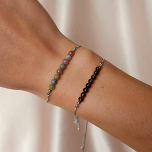 Puede incluir: Dos pulseras ajustables con cordones plateados y cuentas de piedras preciosas. Una pulsera tiene cuentas marrones y la otra tiene cuentas multicolores.