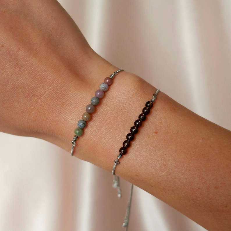 Puede incluir: Dos pulseras ajustables con cordones plateados y cuentas de piedras preciosas. Una pulsera tiene cuentas marrones y la otra tiene cuentas multicolores.