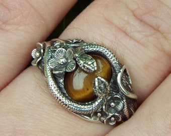 May include: A silver ring with a tiger's eye stone set in a snake and floral design.