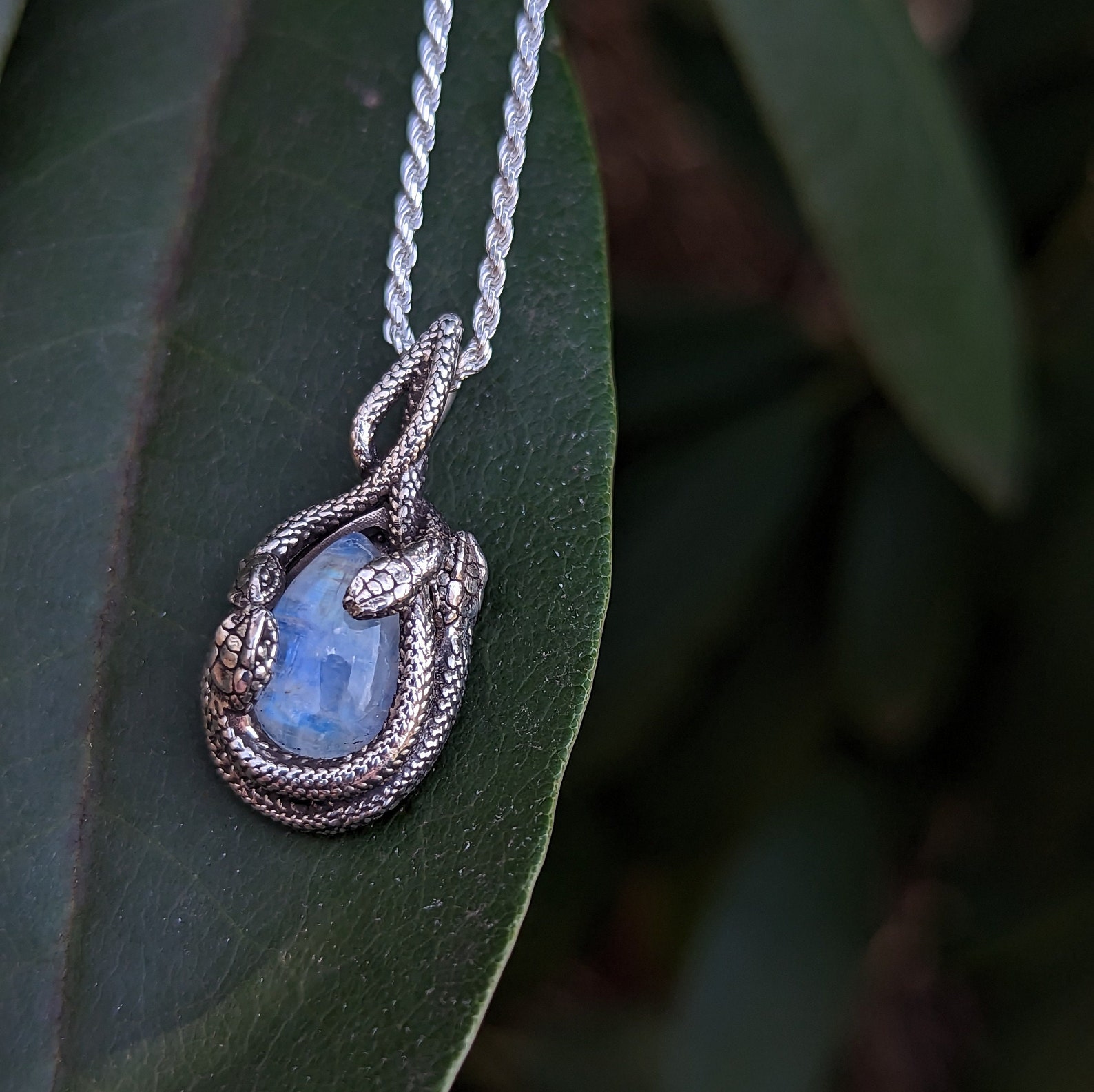 Close-up of sterling silver snake pendant with moonstone, displayed on a dark green leaf.