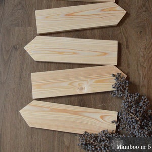 Könnte beinhalten: Fünf unfertige Holzpfeile, die in einem versetzten Muster auf einem braunen Holzgrund angeordnet sind. Die Schilder sind alle gleich groß und gleich geformt, mit einer spitzen Spitze und einer flachen Basis. Das Holz ist hellbraun, mit einem natürlichen Maserungsmuster. Die Schilder sind perfekt, um jedem Zuhause oder Garten eine rustikale Note zu verleihen.