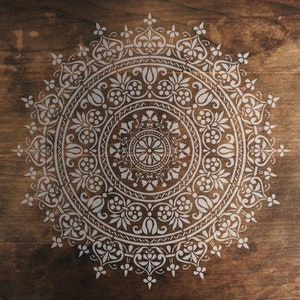 Peut inclure: Un pochoir de mandala blanc sur un fond en bois brun. Le mandala est un motif circulaire avec des détails complexes.