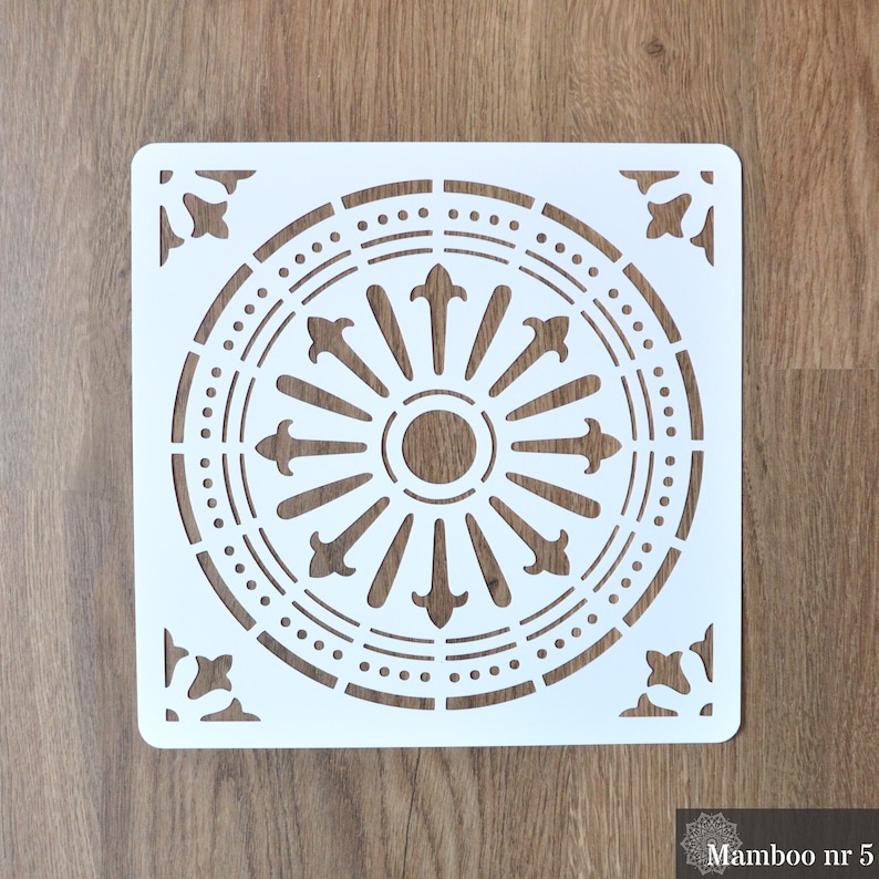 May include: White plastic stencil with a circular design featuring a repeating pattern of dots and arrows. The stencil is square shaped and has a decorative corner design.