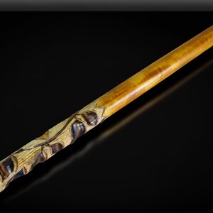 May include: A wooden walking stick with a carved design of leaves and berries. The stick is brown and yellow and has a smooth finish.