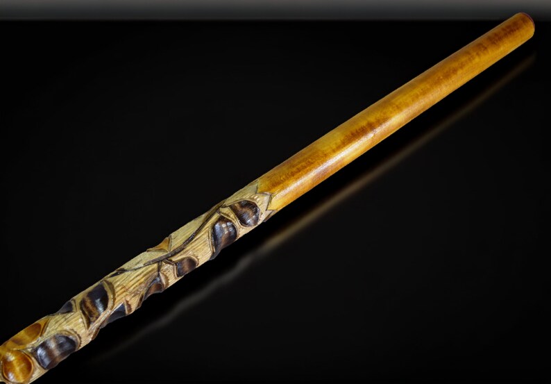 May include: A wooden walking stick with a carved design of leaves and berries. The stick is brown and yellow and has a smooth finish.