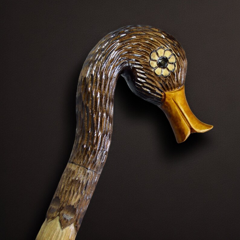 May include: A wooden walking stick carved in the shape of a duck's head. The duck's head is painted brown with a gold beak and a white flower design on the eye.