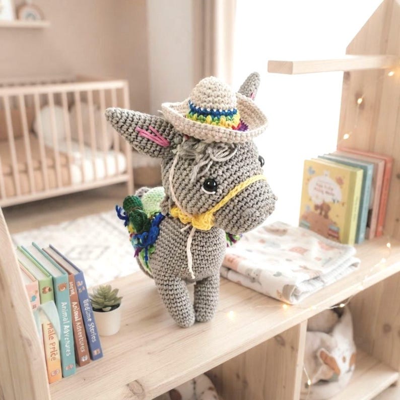 Lifestyle photo of a finished crochet donkey amigurumi toy displayed on a wooden shelf alongside children's books and toys.