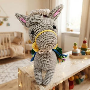 Front view close-up of a crocheted plush donkey amigurumi wearing a yellow bridle and Mexican sombrero in a nursery room decor.