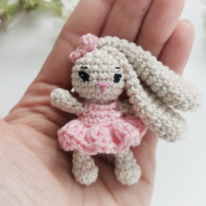 May include: A handmade crochet bunny doll with a pink dress and bow. The bunny has long, floppy ears, black eyes, and a pink nose. The doll is small and appears to be made of soft yarn. The overall aesthetic is cute and whimsical.