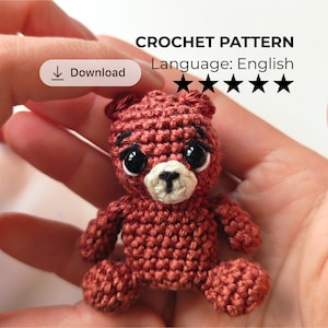 May include: A small, rust-colored crocheted bear with black plastic eyes and a cream-colored muzzle featuring a stitched black nose. The image includes the text CROCHET PATTERN, Language: English, a download button icon, and five black star symbols.