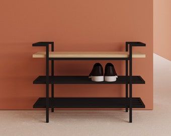 May include: A black metal shoe rack with three shelves and a light wood top. The rack is against a peach-colored wall and has a pair of black and white shoes on the middle shelf.