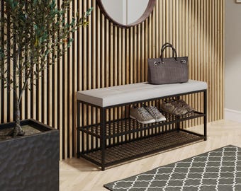 May include: A rectangular entryway bench featuring a black metal frame with a grid-patterned lower shelf and a light gray tufted upholstered seat. The bench holds a dark gray textured handbag and two pairs of sneakers on the shelf.