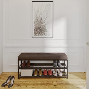 Puede incluir: Un banco rectangular tapizado en marrón oscuro con una parte superior capitoné y dos estantes metálicos de listones para guardar zapatos. El banco contiene varios pares de zapatos y una caja blanca, mientras que un par de tacones negros descansa.