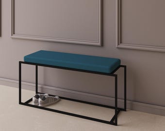 May include: A rectangular bench featuring a teal upholstered seat cushion supported by a thin black metal frame. The base of the bench includes a lower shelf where a pair of gray and white athletic sneakers are placed for storage.