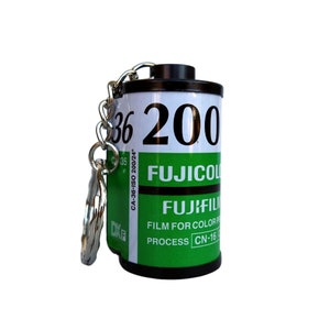 Puede incluir: Un llavero de color negro y verde en forma de cartucho de película con el texto "36 200", "CA-36-ISO 200/24°", "FUJICOL", "FUJIFIL", "FILM FOR COLOR", "PROCESS CN-16" y "DXE".