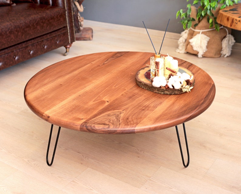 May include: A round wooden coffee table with a natural wood finish and black hairpin legs. The table has a decorative wooden tray with candles and other decorative items on top.