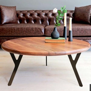May include: A round wooden coffee table with a dark brown wood top and black metal legs. The legs are shaped like a Y. The table is sitting in front of a brown leather sofa.