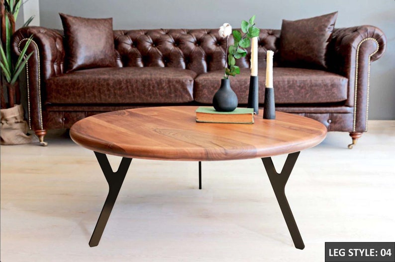 May include: A round wooden coffee table with a dark brown wood top and black metal legs. The legs are shaped like a Y. The table is sitting in front of a brown leather sofa.