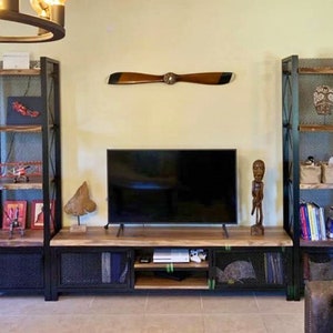 May include: A black metal TV stand with wood shelves and a wood top. The stand has two open shelves on each side and two closed cabinets with wire mesh doors. There is a TV on the top shelf and a wooden propeller on the wall behind the stand.