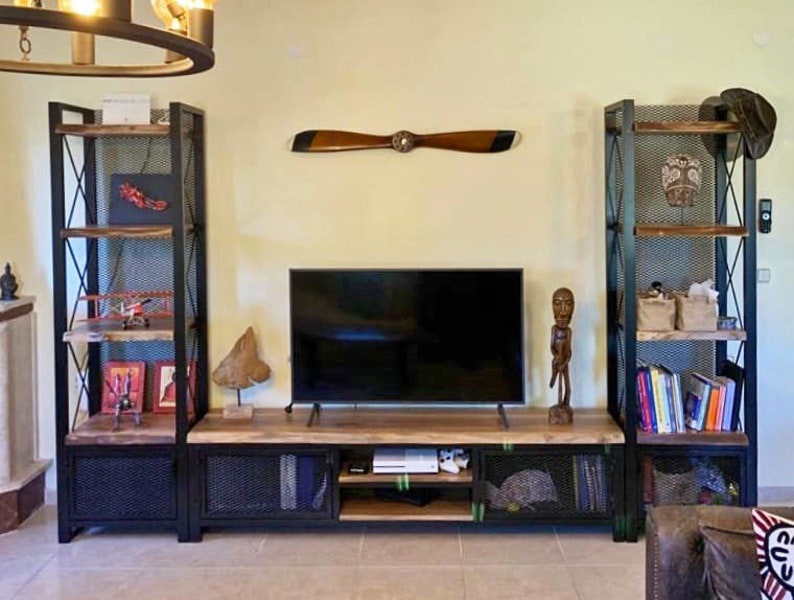 May include: A black metal TV stand with wood shelves and a wood top. The stand has two open shelves on each side and two closed cabinets with wire mesh doors. There is a TV on the top shelf and a wooden propeller on the wall behind the stand.