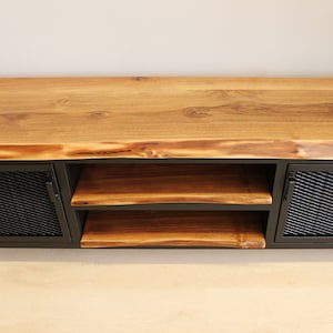 May include: A wooden TV stand with a live edge top and two black metal doors with mesh inserts. The stand has two shelves.