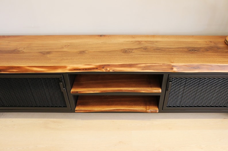 May include: A wooden TV stand with a live edge top and two black metal doors with mesh inserts. The stand has two shelves.