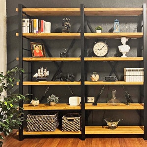 Pode incluir: Uma estante de metal preto com prateleiras de madeira. As prateleiras est&atilde;o cheias de v&aacute;rios itens, incluindo livros, um rel&oacute;gio, um vaso e uma moldura. A estante est&aacute; contra uma parede preta.
