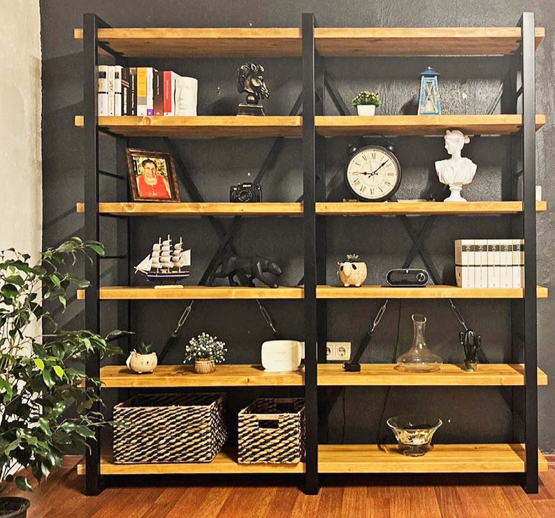 Pode incluir: Uma estante de metal preto com prateleiras de madeira. As prateleiras est&atilde;o cheias de v&aacute;rios itens, incluindo livros, um rel&oacute;gio, um vaso e uma moldura. A estante est&aacute; contra uma parede preta.
