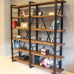 Pode incluir: Uma estante alta de estilo industrial com estrutura de metal preto e prateleiras de madeira. As prateleiras est&atilde;o cheias de v&aacute;rios itens, incluindo livros, plantas e objetos decorativos.