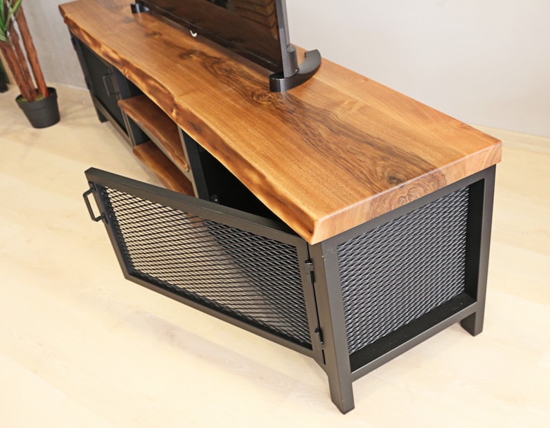 May include: A wooden and metal TV stand with a live edge top and black metal mesh doors. The doors are open, revealing a shelf inside.