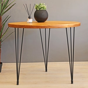 K&ouml;nnte beinhalten: Ein runder Holztisch mit einer nat&uuml;rlichen Holzoptik und schwarzen Haarnadelbeinen. Der Tisch hat einen Durchmesser von 76 cm und eine H&ouml;he von 76 cm.